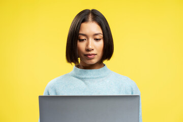 Portrait of pensive serious Asian woman using laptop with stylish hairstyle typing on keyboard