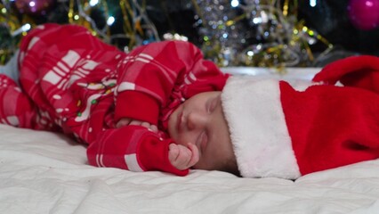 Obraz na płótnie Canvas Sleeping, two week old, newborn, baby boy wearing a crocheted Santa hat with snowman plush toy. Christmas or New Year, holidays at home. decorated Christmas tree