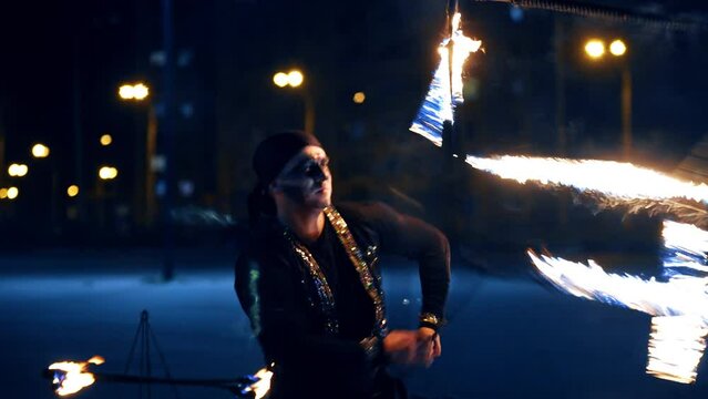 Man in costume turns a big burning cube around himself. Artist performs fire show to the public at night.