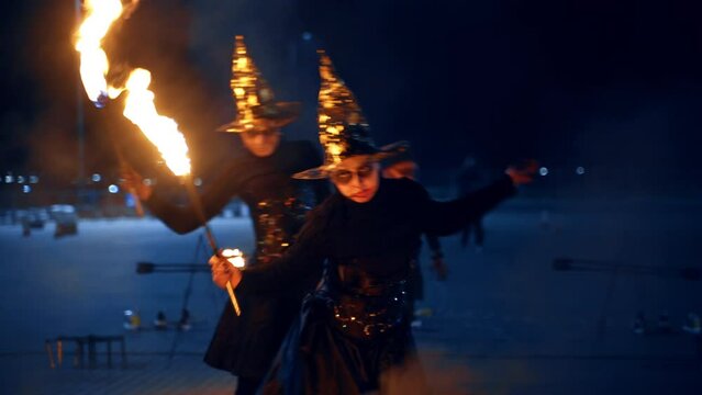 Female actors perform fire show wearing witch costumes. Artistic band shows the fire spectacle outdoors.