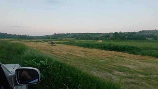 Tractor standing on agricultural field recorded from a car, hand in right side mirror