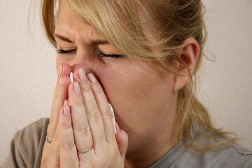 Close up of sick woman sneezing in a tissue at home