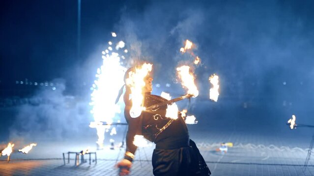 Man dancing fearlessly with burning object. Artist rotates burning stick at night. Fireworks at backdrop.