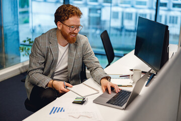 Smiling male manager working on laptop while sitting the desk on office background