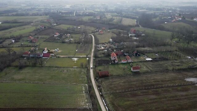 Car drives on dirt road in flooded countryside with few old houses in Ub, Serbia