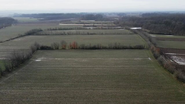 Flight above empty agricultural fields with frozen puddles in Ub, Serbia in winter
