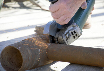 male hands hold a working power tool for cutting metal. a worker is trying to cut a pipe. a sheaf...
