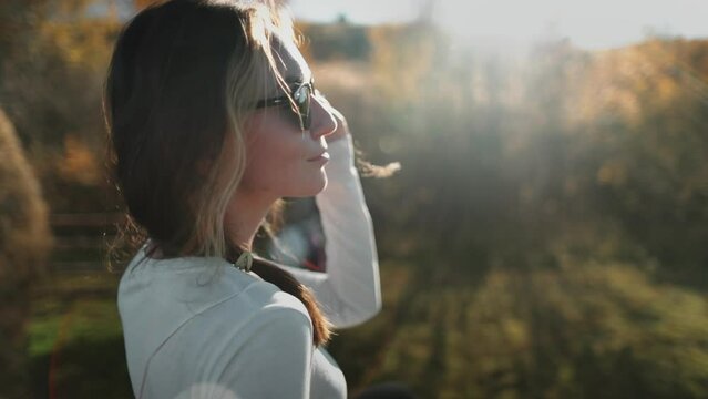 Woman put on sunglasses outdoor sunset nature landscape. Girl enjoy countryside rural autumn scene. Young female relax, have rest, meditate. Active lifestyle travel on holiday vacation. Slow motion