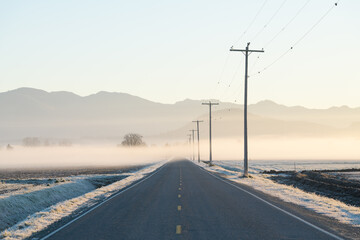 Thin layer of fog across Skagit Valley road at sunrise with telephone poles and lines leading into distance of frosty scene - Powered by Adobe