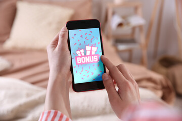 Bonus gaining. Woman using smartphone indoors, closeup. Illustration of gift boxes, word and falling confetti on device screen - obrazy, fototapety, plakaty