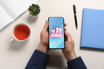 Bonus gaining. Man holding smartphone at white table, top view. Illustration of gift boxes, word...