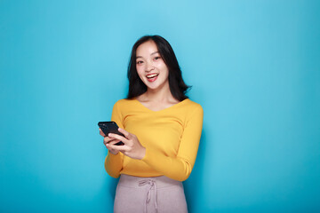 A woman has a pink background as a backdrop for a single portrait, smiling and holding a cell phone...