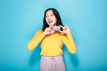 Asian woman posing with a credit card, Portrait of a beautiful young woman in a light blue background, happy and smile, posting in stand position.