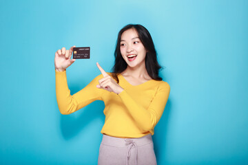 Naklejka premium Asian woman posing with a credit card, Portrait of a beautiful young woman in a light blue background, happy and smile, posting in stand position.