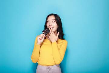 Asian woman posing with a credit card, Portrait of a beautiful young woman in a light blue background, happy and smile, posting in stand position.