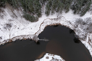 Aerial view over the winter forest growing on the river bend, high contrast vertical view of the...