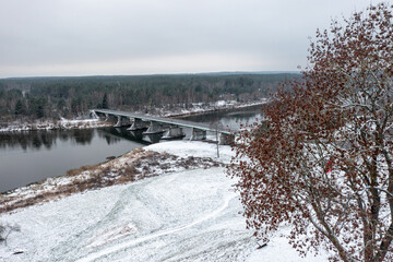 Aerial view of the bridge over the river and forest in a cloudy day. A bridge andmeadow is partly covered witha trea; shot made in Lithuania