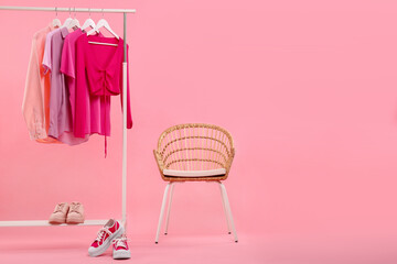 Rack with different stylish women`s clothes, sneakers and armchair on pink background, space for...