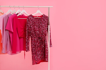 Rack with different stylish women`s clothes on pink background, space for text