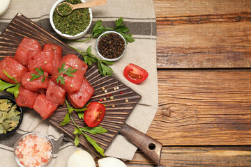 Raw beef meat and different ingredients for cooking delicious goulash on wooden table, flat lay. Space for text