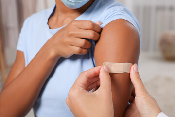 Doctor putting adhesive bandage on young woman's arm after vaccination indoors, closeup
