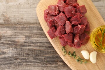 Pieces of raw beef meat, oil and garlic on wooden table, top view. Space for text