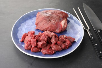 Plate with pieces of raw beef meat, knife and fork on grey textured table, closeup