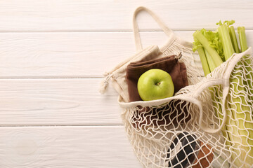 Net bag with different items on white wooden table, top view and space for text. Conscious consumption