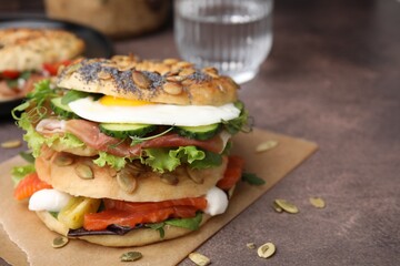 Tasty bagel with cured ham, egg, salmon and vegetables on brown table, closeup. Space for text