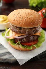 Tasty hamburger with patties, cheese and vegetables on wooden table