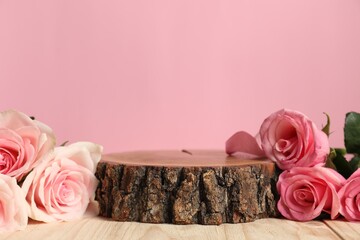 Stylish presentation of product. Beautiful roses and stump on wooden table against pink background,...
