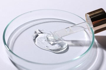 Petri dish with sample of cosmetic serum and pipette on white background, closeup