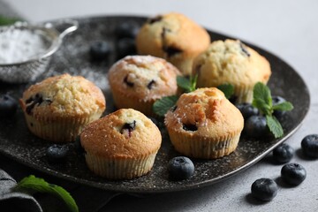 Delicious muffins with powdered sugar, blueberries and mint on light grey table, closeup