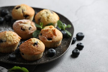 Delicious muffins with powdered sugar, blueberries and mint on light grey table, closeup