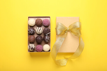 Open box with delicious chocolate candies on yellow background, top view