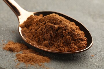 Spoon with cinnamon powder on grey table, closeup