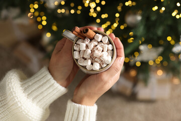 Woman holding cup of delicious Christmas cocoa with marshmallows and cinnamon sticks against...