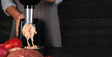 Woman making chicken mince with electric meat grinder at black table, closeup. Banner design with...