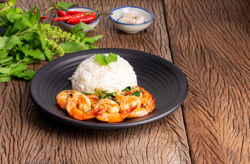 Stir-fried shrimp with basil Thai street food, arranged on a black plate Spicy Thai food placed on a wooden table. Top view with space to copy text.