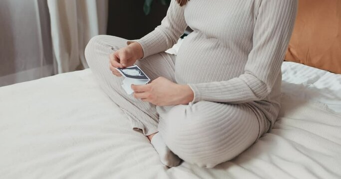 Young attractive pregnant woman holds her ultrasound photos close to her heart, imagining all the possibilities and dreams for her unborn child. Anticipation and hope concept.