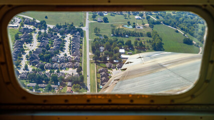 looking out left window of vintage military bomber during a left bank with a housing complex visible below