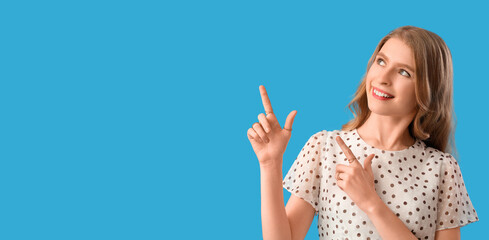 Young woman pointing at something on blue background with space for text