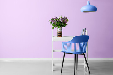 Beautiful lilac flowers on table and armchair near lilac wall in room. Banner for design