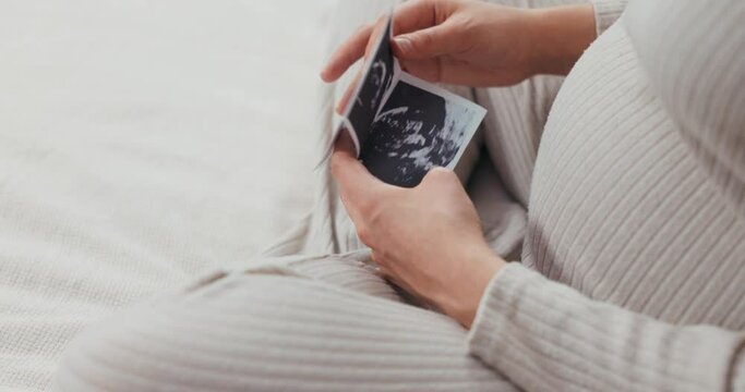 Pregnancy joy concept woman holds up her ultrasound images, gazing at them with wonder and excitement for the new life growing inside her.