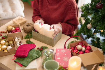 Fototapeta na wymiar Young asian woman in sweater with happiness packing gift into cardboard box to wrapping christmas present while prepare ornaments to celebrate for christmas festive holiday and winter seasons at home
