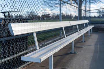 An empty aluminum bench in a baseball dugout at a public park.