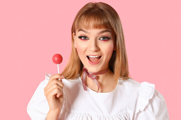 Young woman in doll clothes with lollipop on pink background, closeup