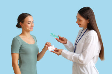 Female gynecologist giving contraceptive pills to patient on blue background