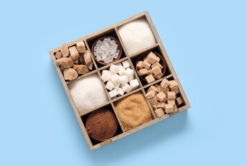 Wooden box with different types of sugar on blue background