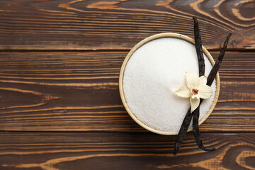Bowl with aromatic vanilla sugar, flower and sticks on wooden background
